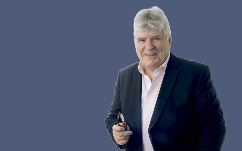 Harmaahiuksinen mies silmälasit kädessä.